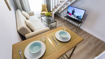 Un comedor con una mesa lista para dos personas, un sofá, una silla y un televisor al fondo.