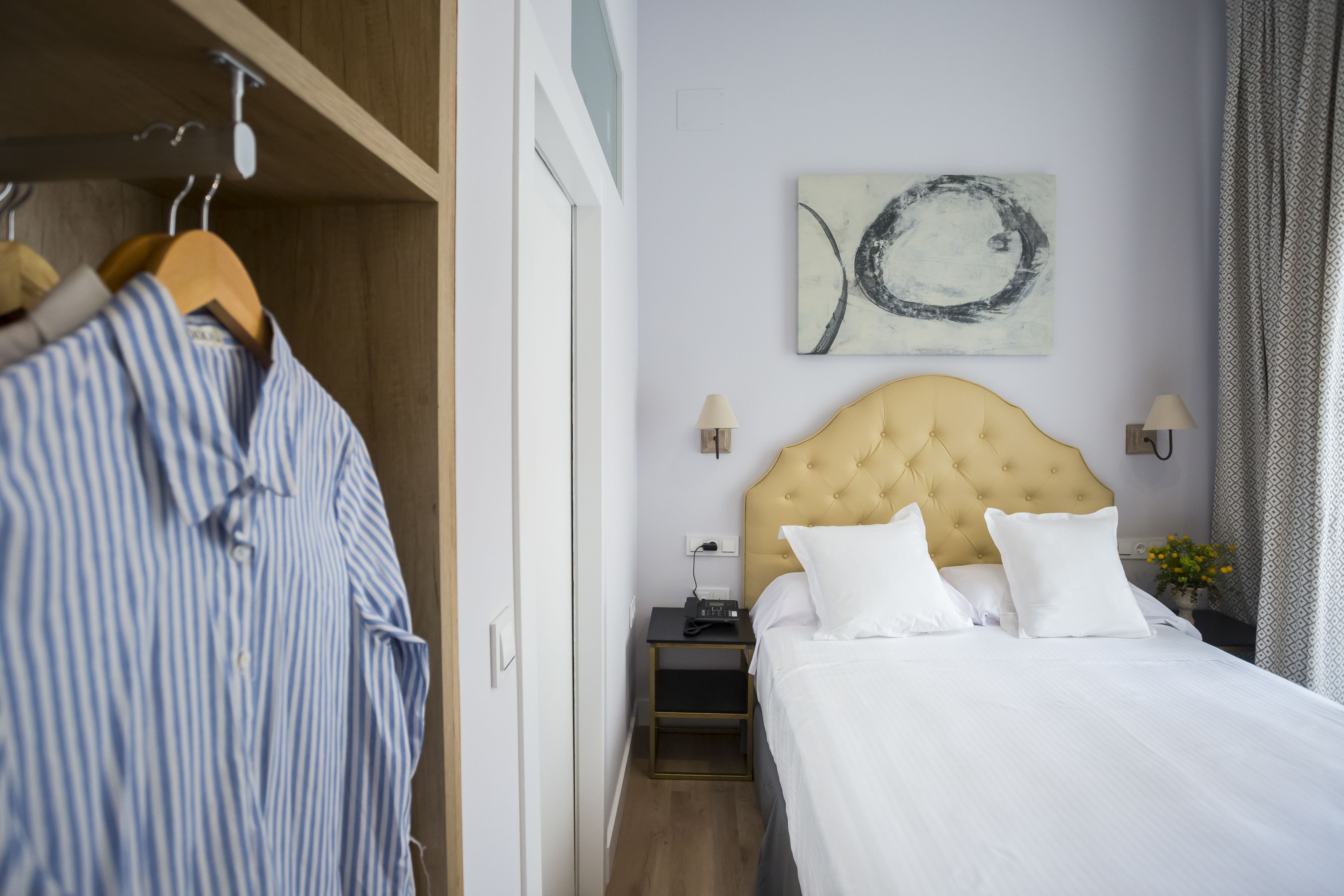 A hotel room with a bed, a nightstand, a lamp, a wall art piece, and a wardrobe.