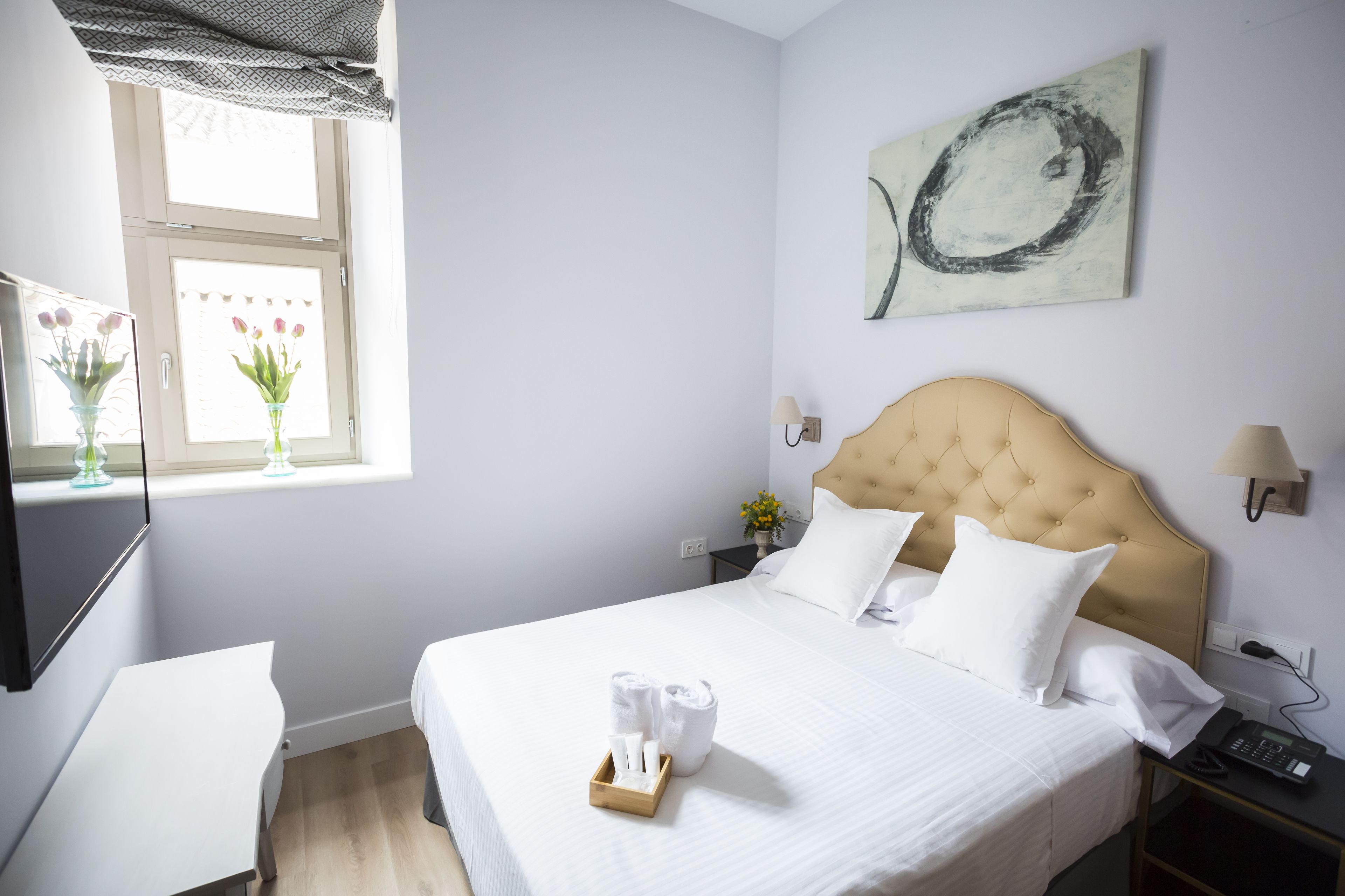 A hotel room with a bed, bedside table, lamp, and artwork on the wall.