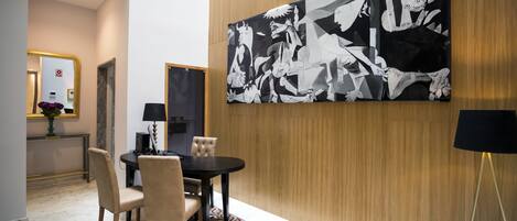 A modern dining area with a black and white abstract painting on the wall, a round table with chairs, and a patterned rug.