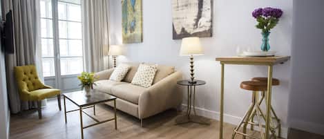 Un salon comprenant un canapé, deux tables d’appoint, un fauteuil jaune et une fenêtre avec des rideaux.