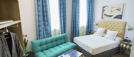 A hotel room with a bed, a sofa, a small table, a wardrobe, and a window with curtains.