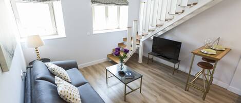 A modern living room with a grey sofa, a coffee table with a vase, a TV, and a staircase.