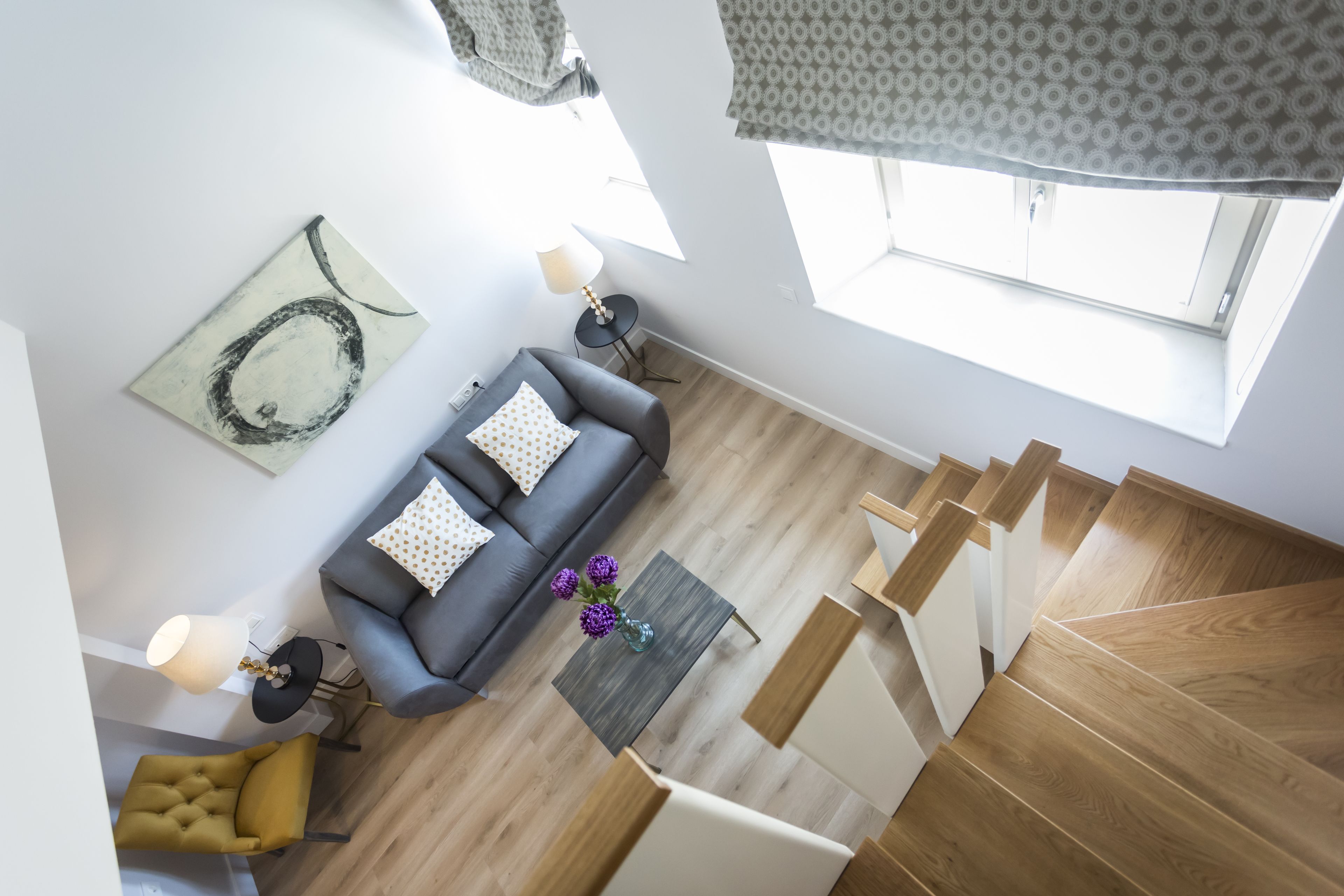 A modern living room with a grey sofa, yellow armchair, and a wooden staircase.