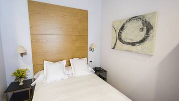 Une chambre d’hôtel avec une tête de lit en bois, un lit avec du linge de lit blanc, une table de chevet avec une lampe, un téléphone et une œuvre d’art murale.