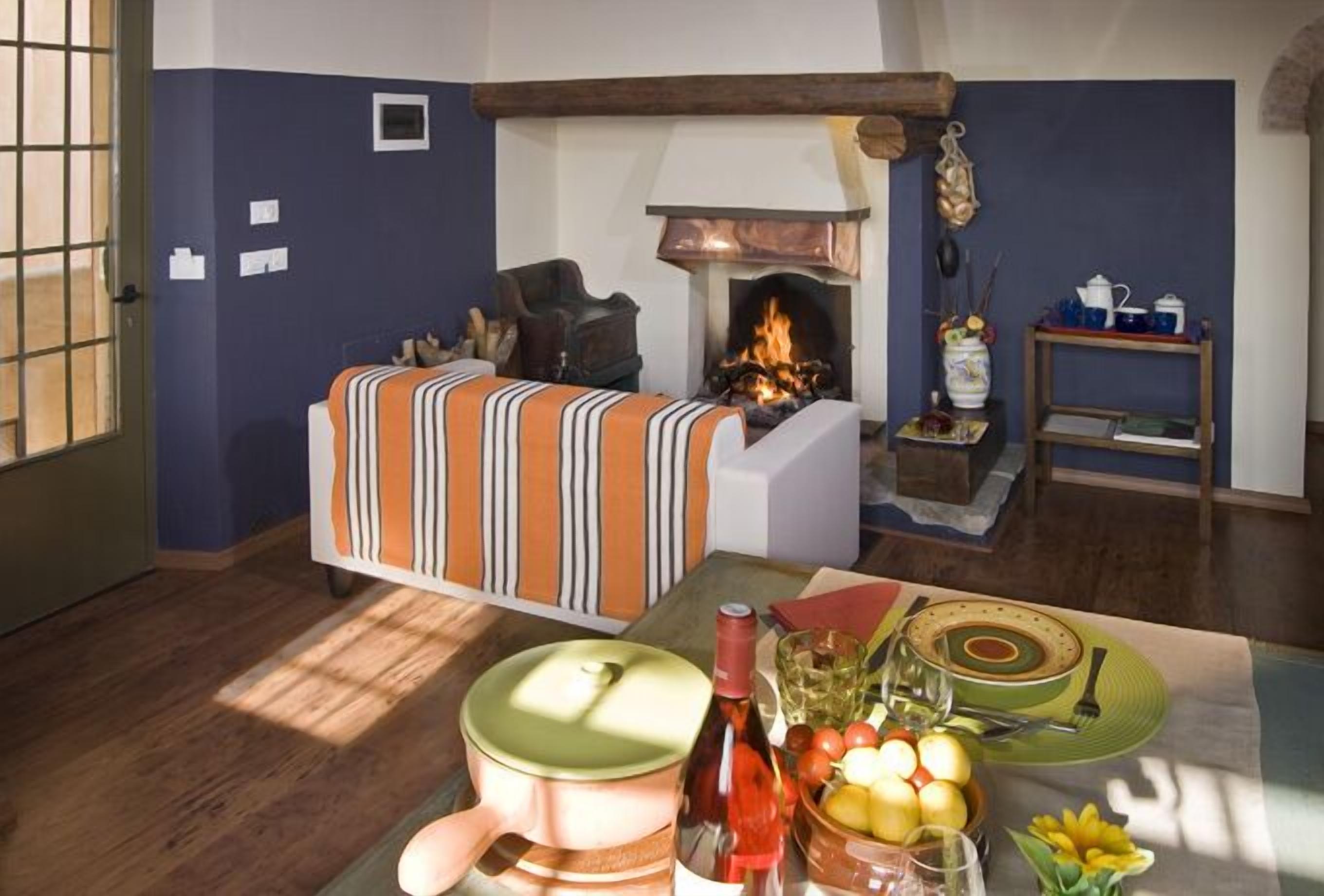 A cozy living room with a fireplace, a sofa, and a dining table set with a bottle, glasses, and fruit.