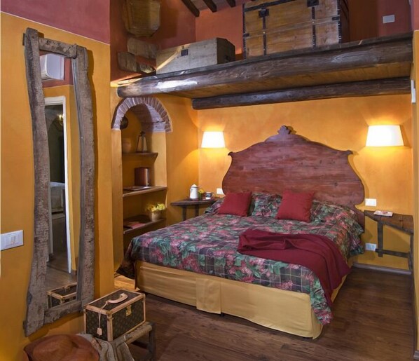 Un dormitorio con cabecera de madera, cama con ropa de cama floral, un espejo grande y un aparador de madera.