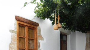 A rustic outdoor seating area with a table and chairs, a wooden window, and hanging planters. - Cosmos Home Lindos (Rhodes)