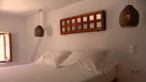 A bedroom with a wooden bed frame, white bedding, and two hanging lamps. - Cosmos Home Lindos (Rhodes)