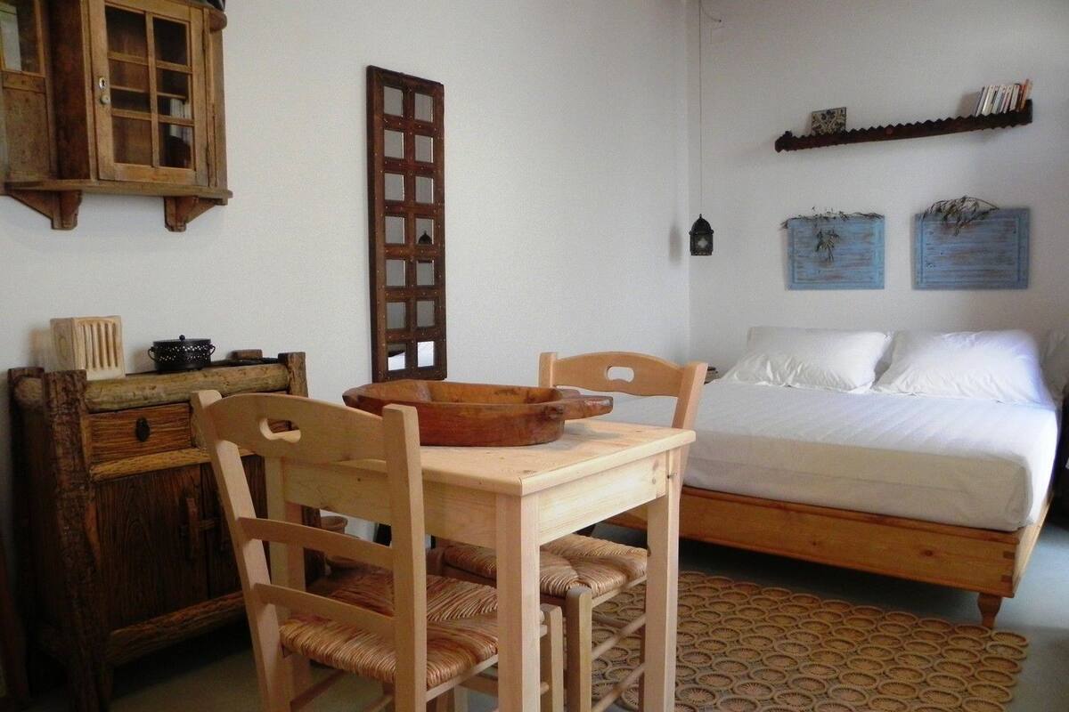 A bedroom with a wooden bed, a wooden chair, a small table, a wooden cabinet, and a wall-mounted shelf.