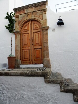 A stone entrance with a wooden double door, a potted plant, and a small step leading up to the door. - Cosmos Home Lindos (Rhodes)