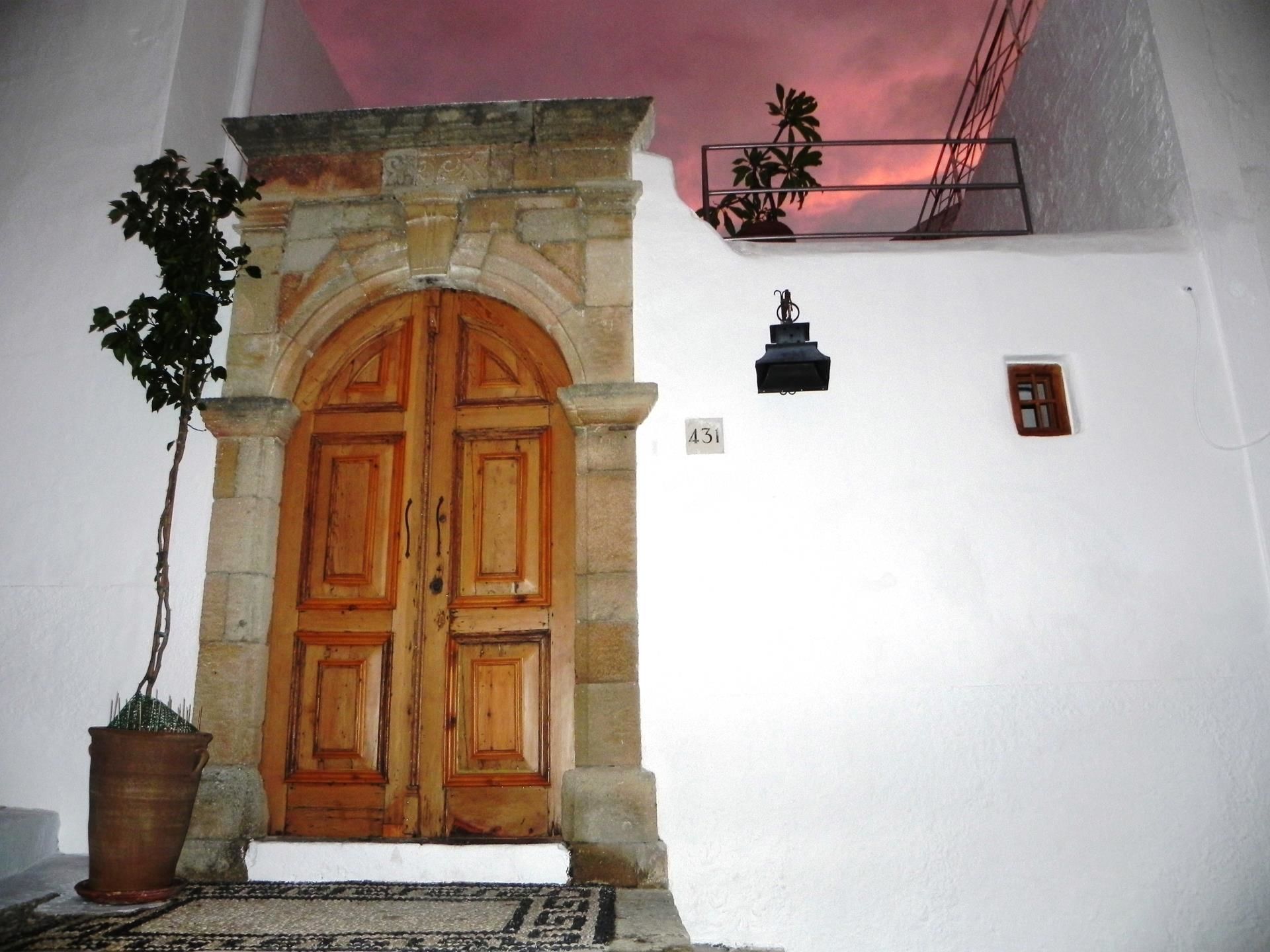 A stone archway entrance with a wooden door, a potted plant, a small wall-mounted light fixture, and a number sign.