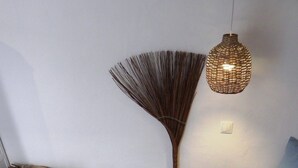 A room with a wooden coffee table, woven baskets, a broom, and a hanging light fixture. - Cosmos Home Lindos (Rhodes)