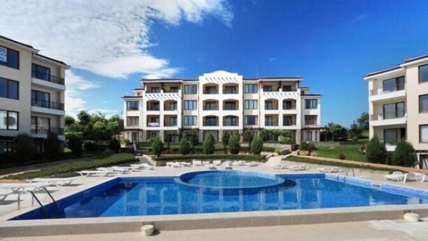 Un hotel con piscina central, varios balcones y abundante vegetación.