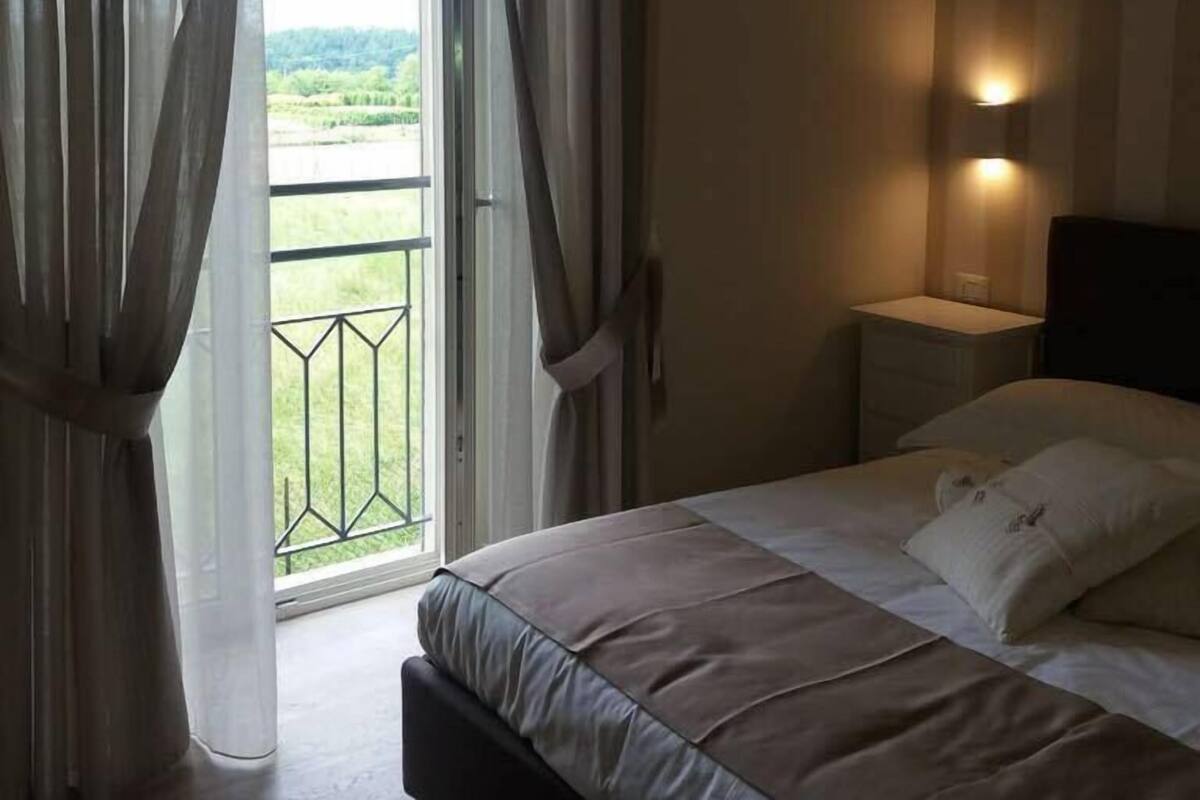 Un dormitorio con cama, mesita de noche, lámpara de pared y balcón con cortinas.