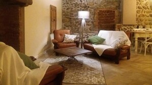Ein gemütliches Wohnzimmer mit einer Steinwand, einem Holztisch und zwei Ledersesseln mit gemusterten Kissen.