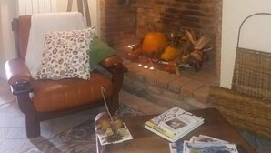 Ein gemütliches Wohnzimmer mit Kamin aus Backsteinen, einem Ledersessel, einem Couchtisch mit Zeitschriften und einer Lampe.