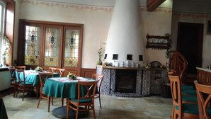 Zona pranzo con sedie e tavoli in legno, un camino e oggetti decorativi sulla mensola.