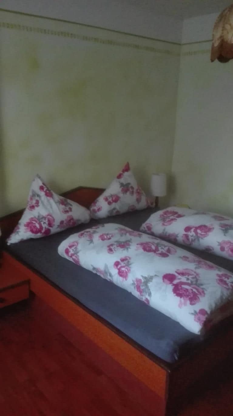 Uma cama com roupa de cama e almofadas florais, uma mesa de cabeceira e uma luminária.