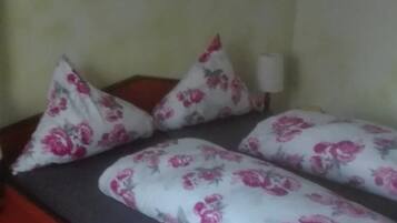 Uma cama com roupa de cama e almofadas florais, uma mesa de cabeceira e uma luminária.