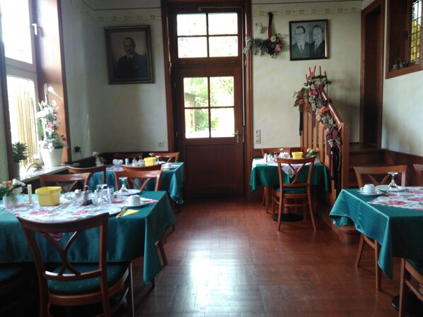 A dining area with tables set for meals, wooden chairs, and a wooden floor.