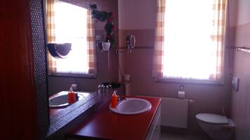 Ein Badezimmer mit einem roten Waschbecken, einem Spiegel, einer Toilette und einem Fenster mit Vorhängen.