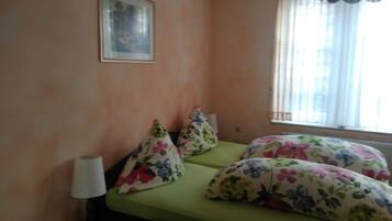 Una habitación pequeña y sencilla con una cama individual, un cuadro en la pared y una ventana con cortinas.