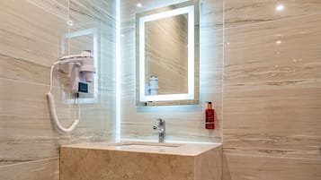 Un baño moderno con tocador de mármol, espejo, secador de pelo y cubo de basura.