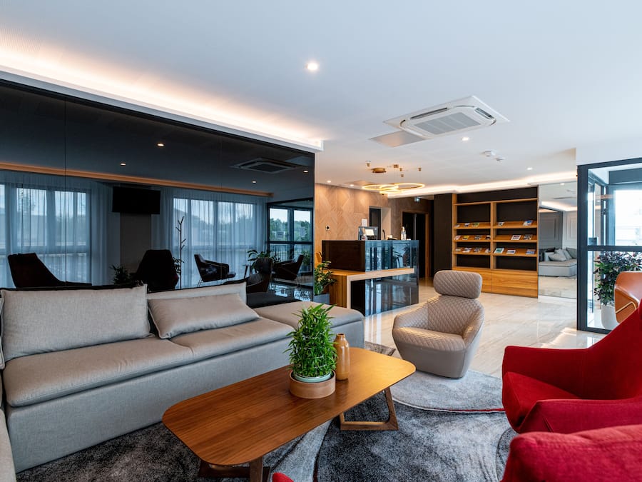 Una sala de estar moderna con un sofá gris, una mesa de centro de madera y un sillón rojo. Se observa una estantería con libros y una planta sobre la mesa de centro.