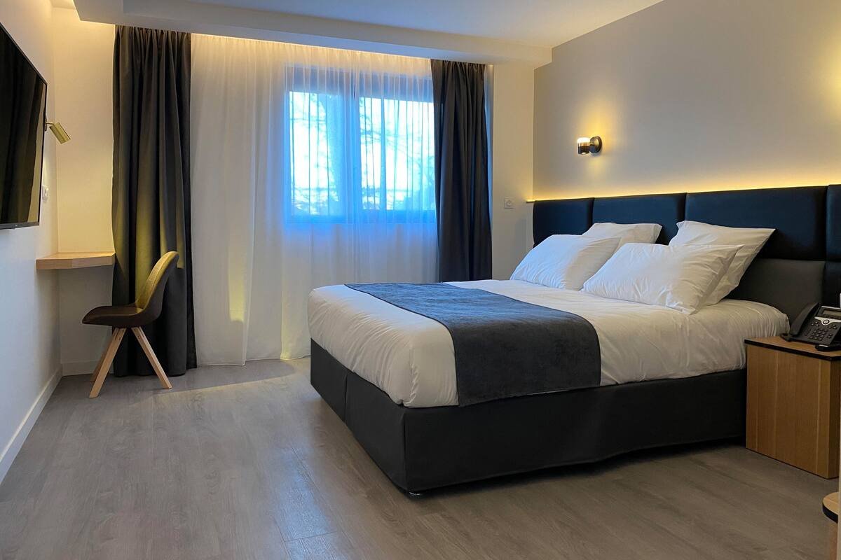 Ein modernes Hotelzimmer mit einem großen Bett, einem Nachttisch mit Telefon und einem Sessel.