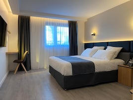 Quarto de hotel moderno com uma cama grande, uma mesinha de cabeceira com telefone e uma cadeira.