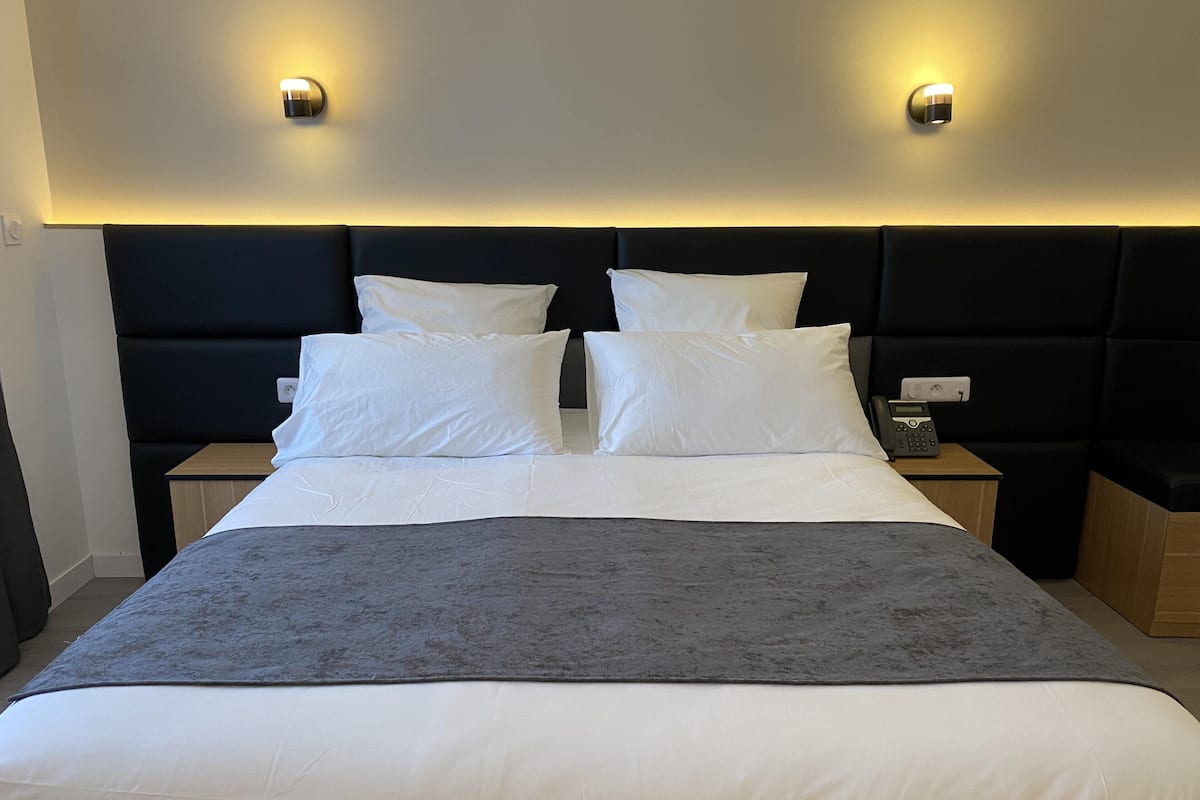 Ein ordentlich bezogenes Bett mit weißen Leinen und einer grauen Tagesdecke, an beiden Seiten flankiert von Nachttischen mit Radio und Telefon.