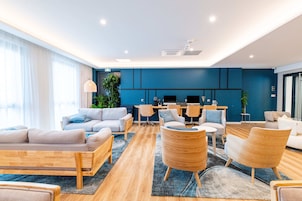 Uma sala de estar moderna com sofás, cadeiras, um espaço de refeições e uma cozinha ao fundo.