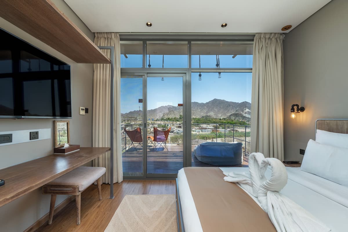 A modern hotel room with a large sliding glass door leading to a balcony with mountain views.