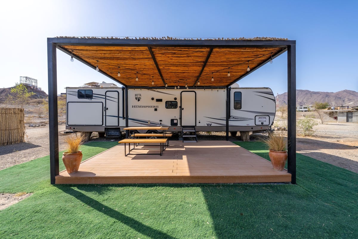 A recreational vehicle with a covered patio area, a picnic table, and potted plants.