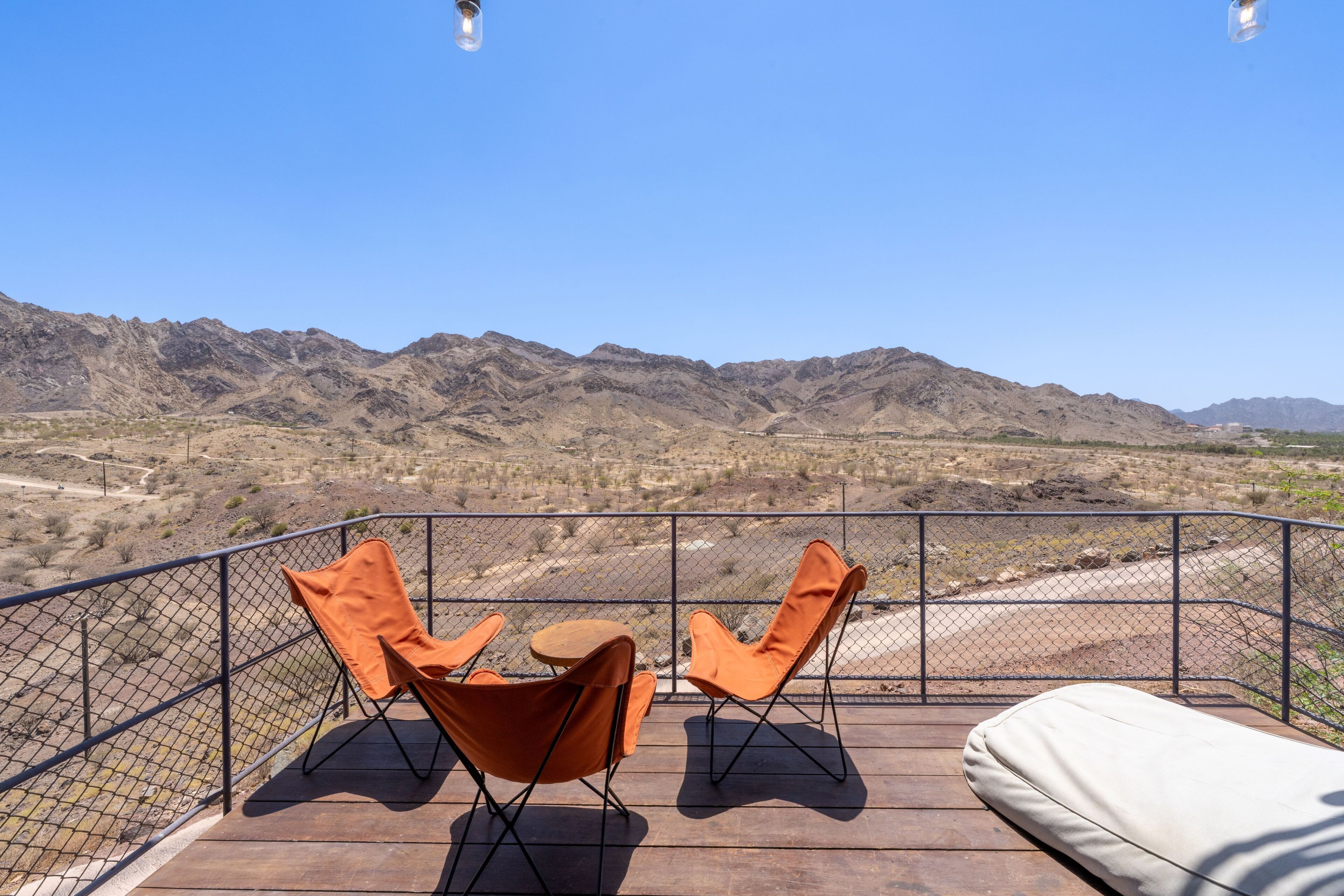 A balcony with two orange chairs and a small table, overlooking a mountainous landscape.
