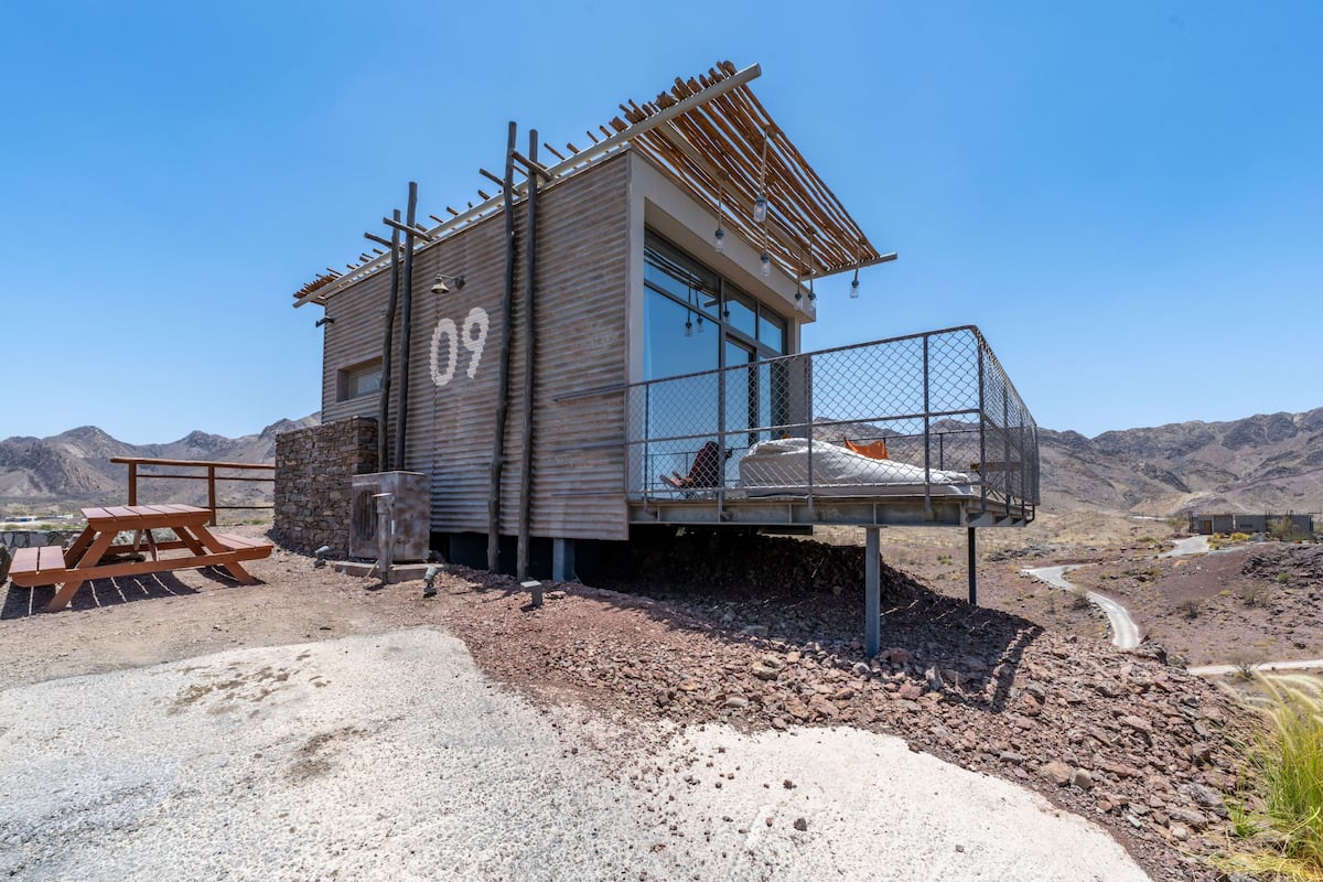 A rustic cabin with a stone exterior, a wooden deck, and a metal railing.