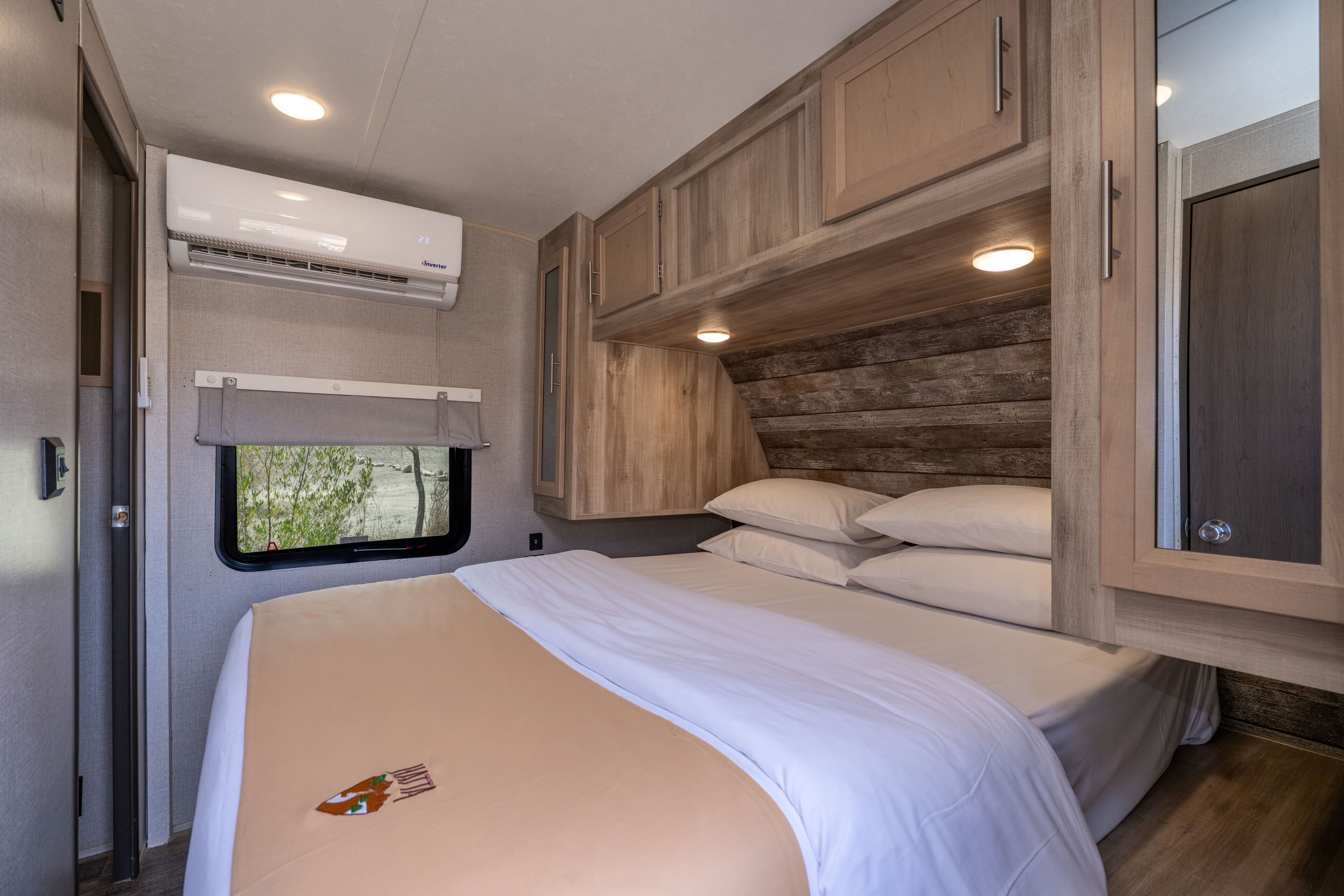 A bedroom with a bed, pillows, a window, and wooden cabinetry.
