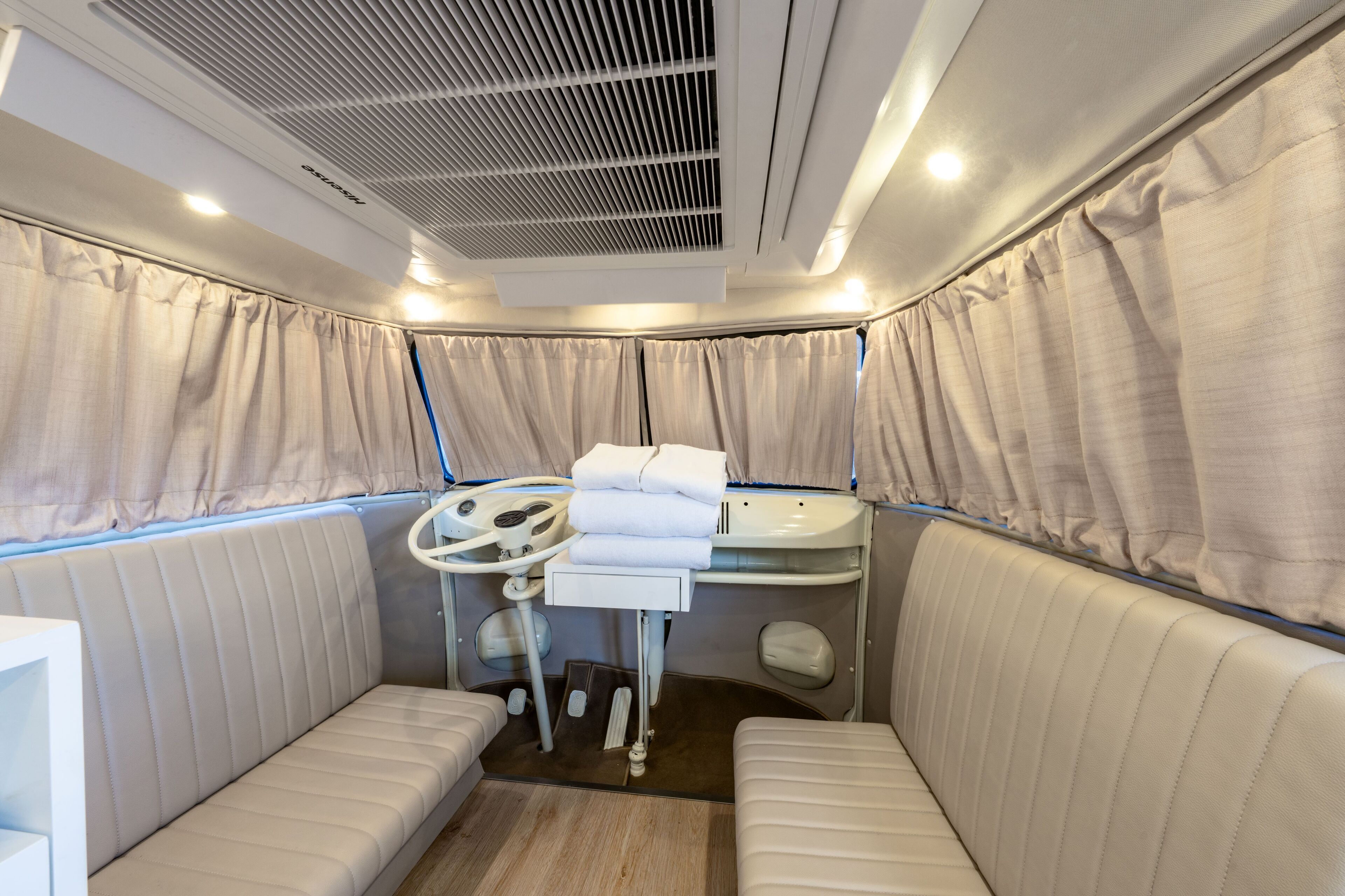 A compact, well-lit room with a cushioned bench seating area, a small table with a control panel, and a ceiling vent.