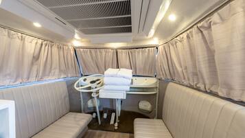 A compact, well-lit room with a cushioned bench seating area, a small table with a control panel, and a ceiling vent.