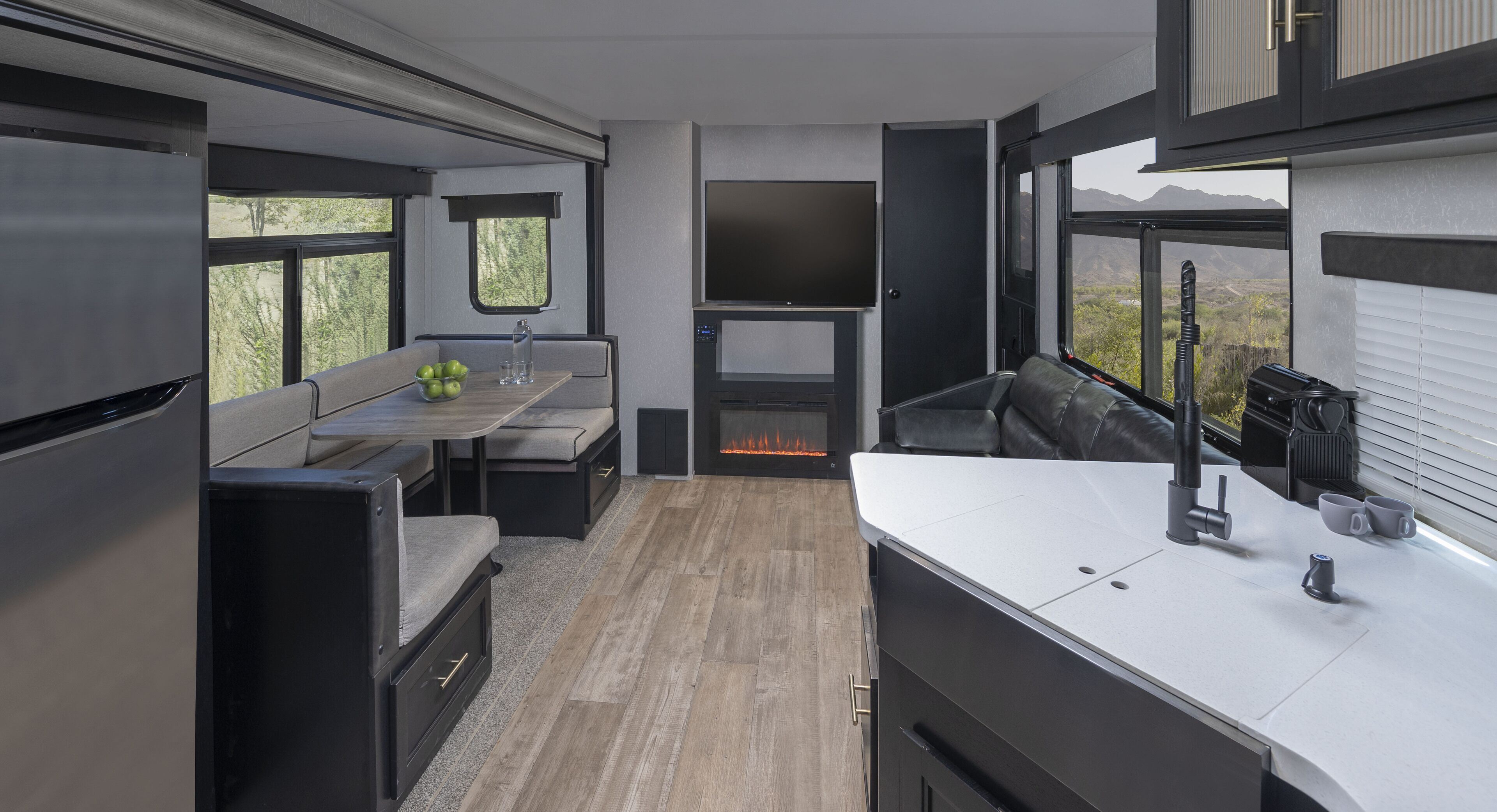 A modern RV kitchen with a dining area, a TV, and a fireplace.