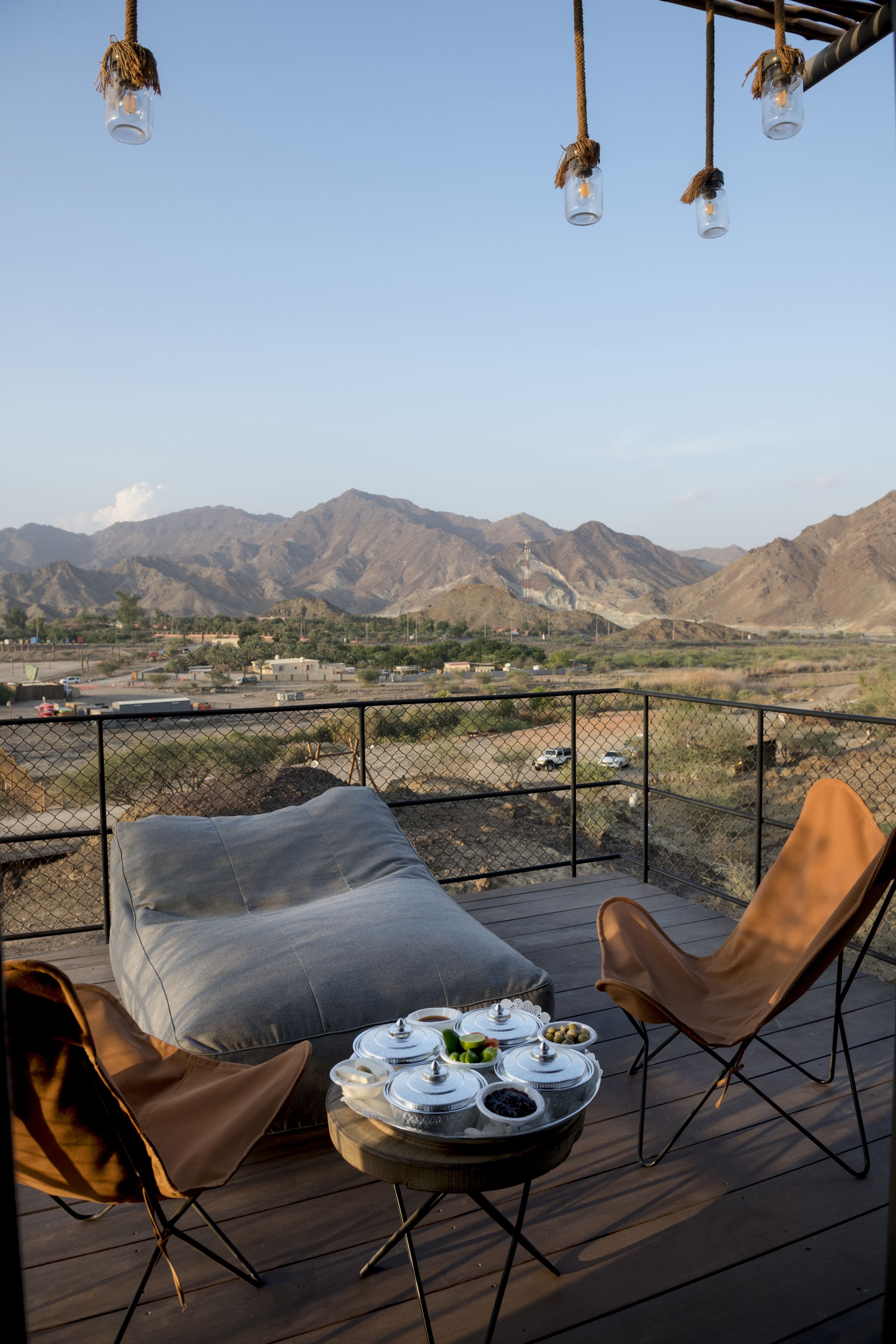 A deck with a view of mountains, a table with food, and two chairs.