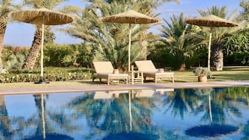 Una piscina al aire libre, sombrillas, sillones reclinables de piscina