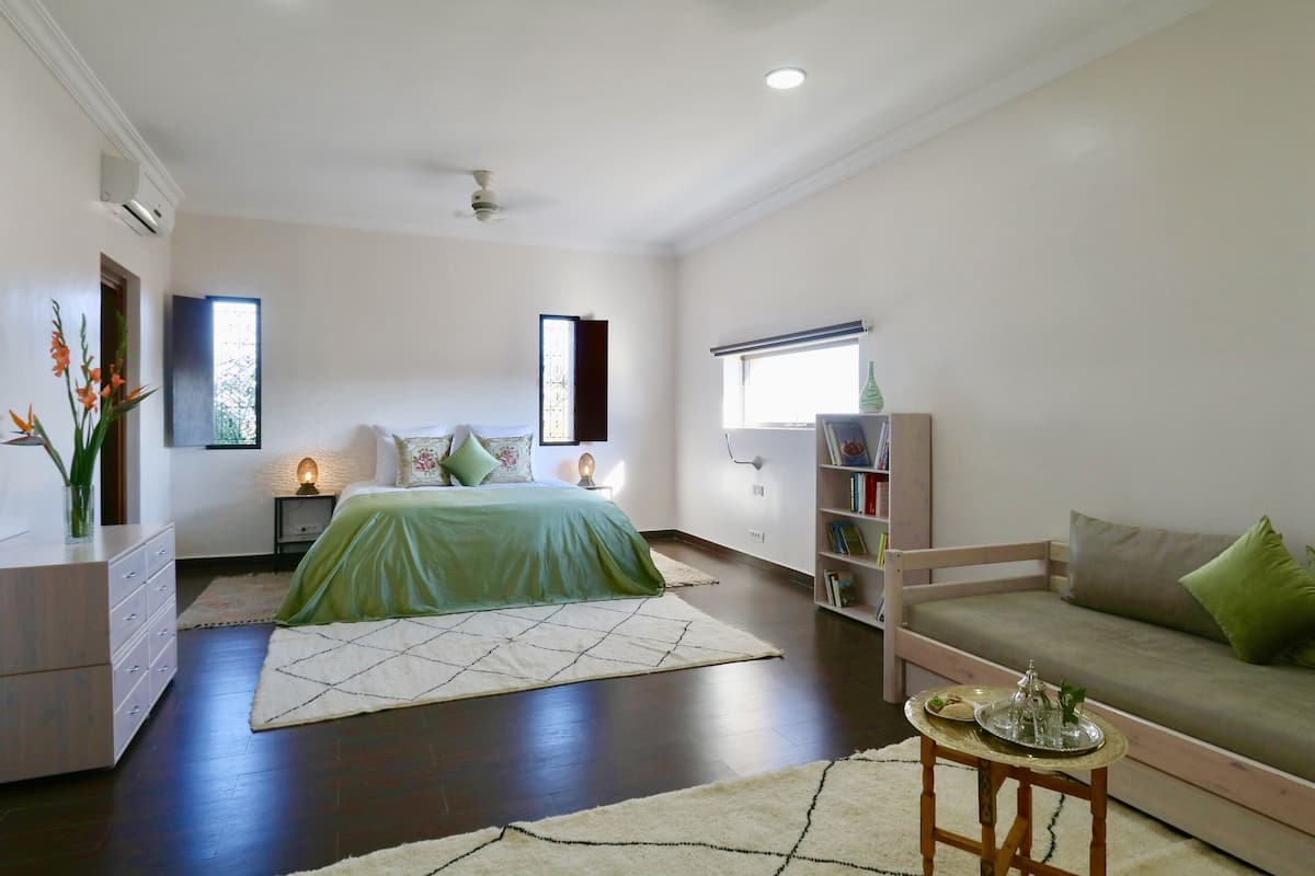 A modern bedroom with a bed, bedside tables, a reading chair, and a bookshelf.