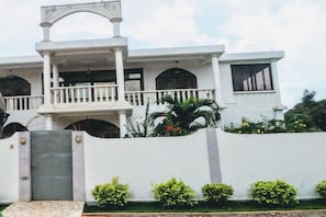 A white two-story house with a balcony, a gated entrance, and a well-maintained garden. - Résidence Soleil Levant (Lomé)