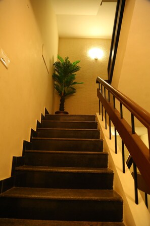 A staircase with wooden steps and a handrail, leading to a landing with a light fixture and a potted plant. - Horizon Inn (Chennai)