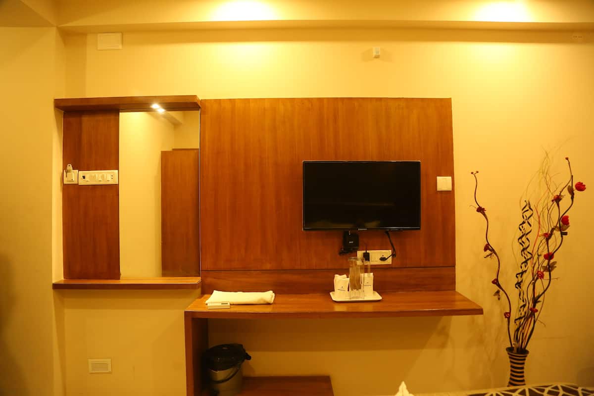 Habitación de hotel con tocador de madera, televisor montado, una mesita con un control remoto y un florero con flores.