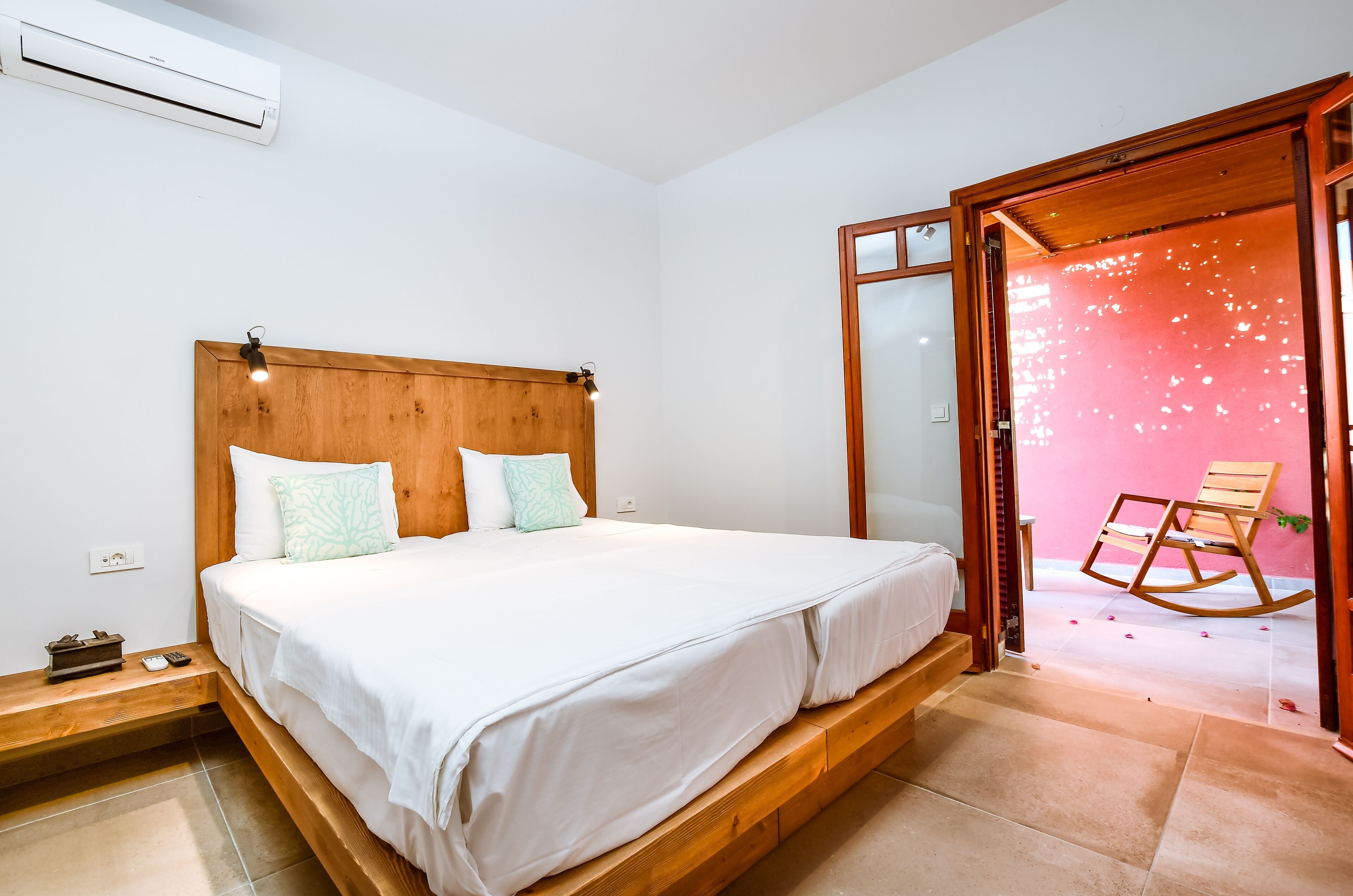 A bedroom with a wooden bed, white bedding, a nightstand, and a rocking chair in a pink room.