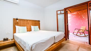 A bedroom with a wooden bed, white bedding, a nightstand, and a rocking chair in a pink room.