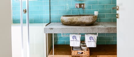 A bathroom with a glass shower door, a stone sink, and a blue tiled wall.